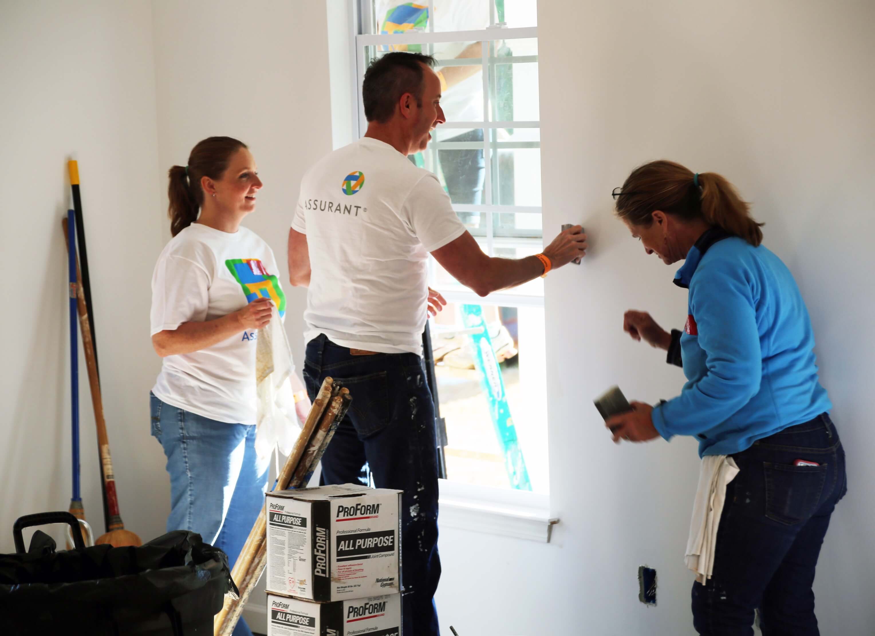 Three Assurant employees working at a Habitat for Humanity build sanding walls